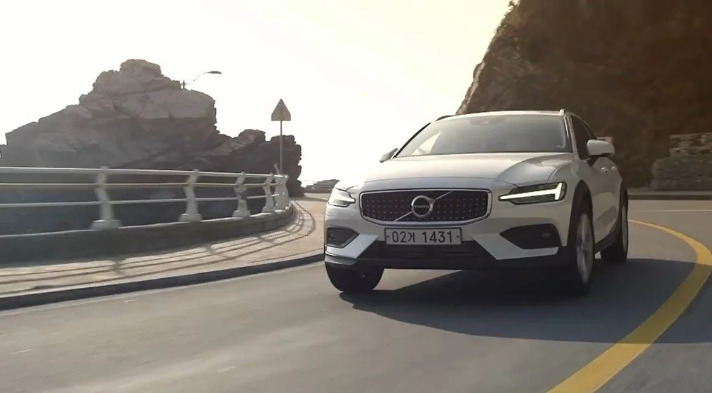Frame from a JTX Media commercial: a white Volvo estate rounding a cliffside coastal road